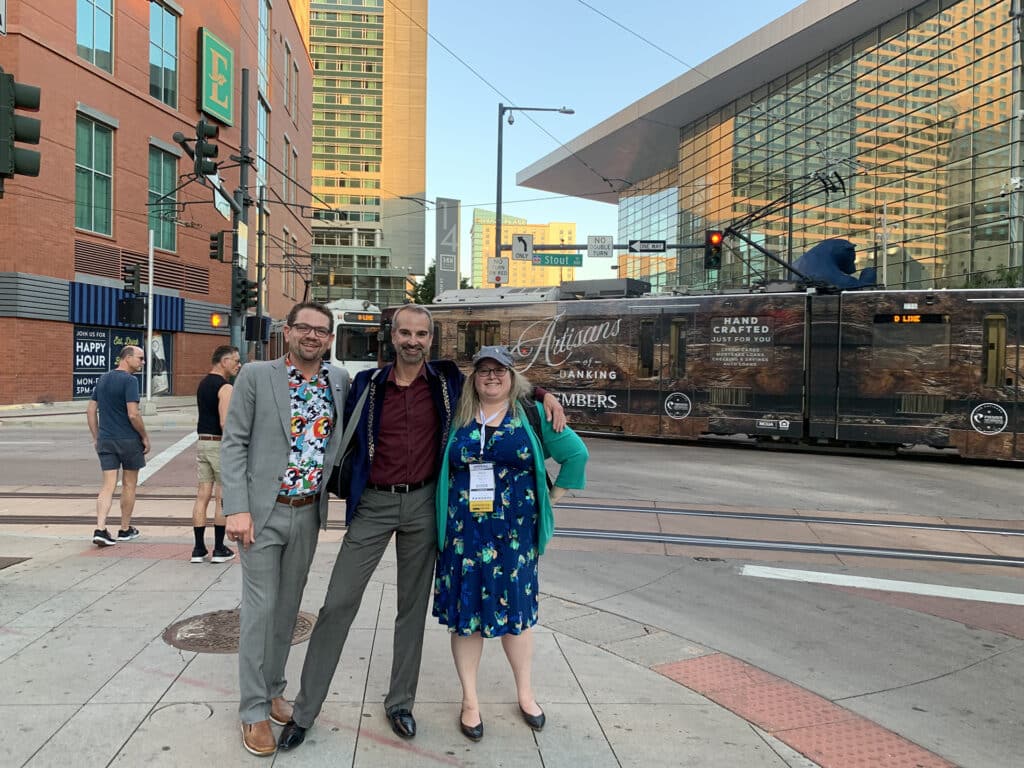 Ethan, Jon, and Allene stand in front of an operating transit line in Denver, Colorado