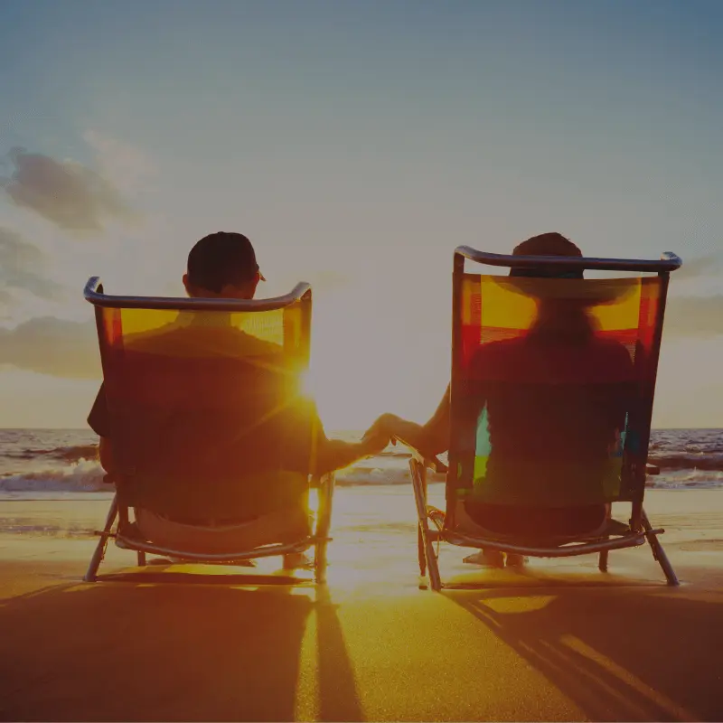 two people lounge at the beach while looking at a sunset.